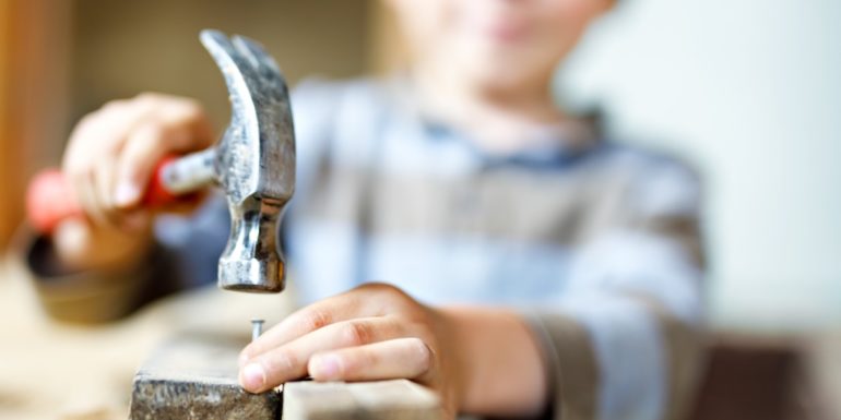 A child about to hammer a nail in to a piece of wood