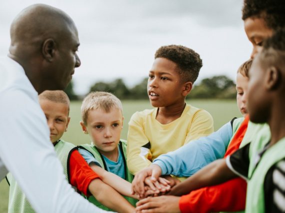 A group of children and an adult placing their hands together in a circle