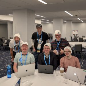A group of six DrupalCon 2026 attendees wearing hats with Drupal CRM logo